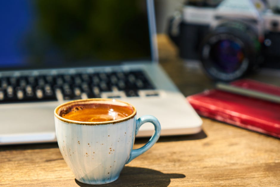A cozy workspace with a cappuccino, laptop, and vintage camera on a wooden desk.